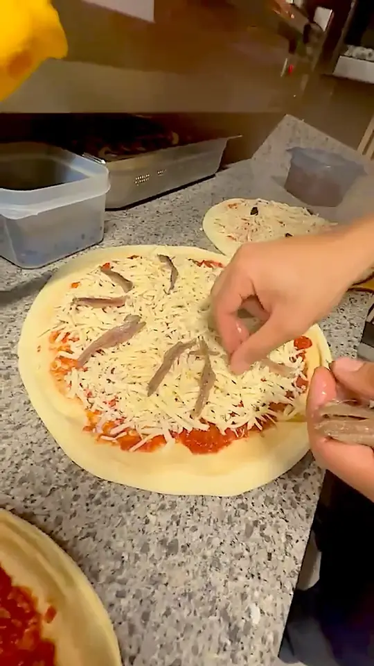 Une pizza garnie à la main sur le plan de travail