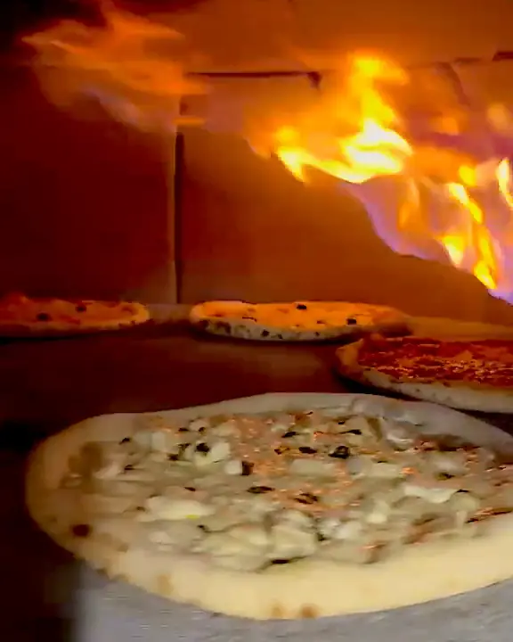 Pizzas qui cuisent sur la pierre du four de la pizzeria, devant les flammes